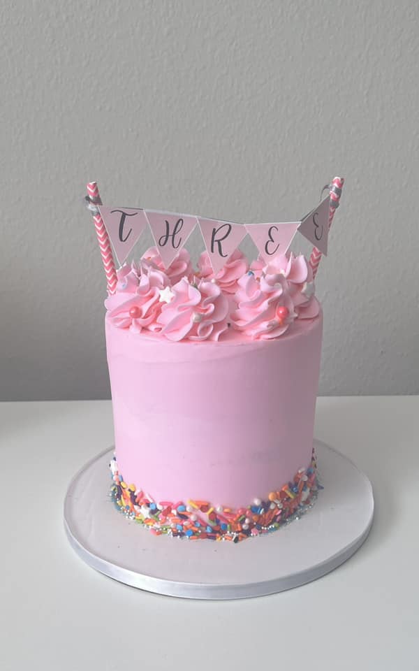 Pink birthday cake with banner topper and sprinkles